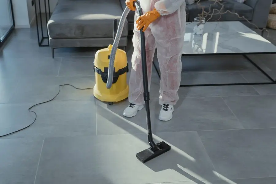 A technician in a white suit running a yellow vacuum in a bright room.