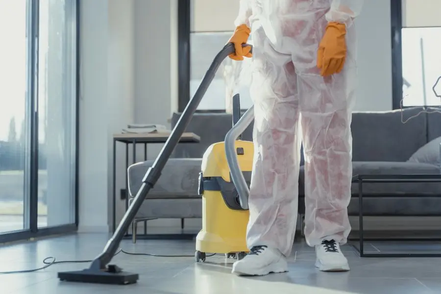 A technician in a white suit with a canister vacuum in a bright room.